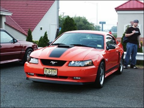 2001 Mercury Grand Marquis - An orange Ford Mustang is parked next to a maroon Ford Mustang at an outdoor car meet.