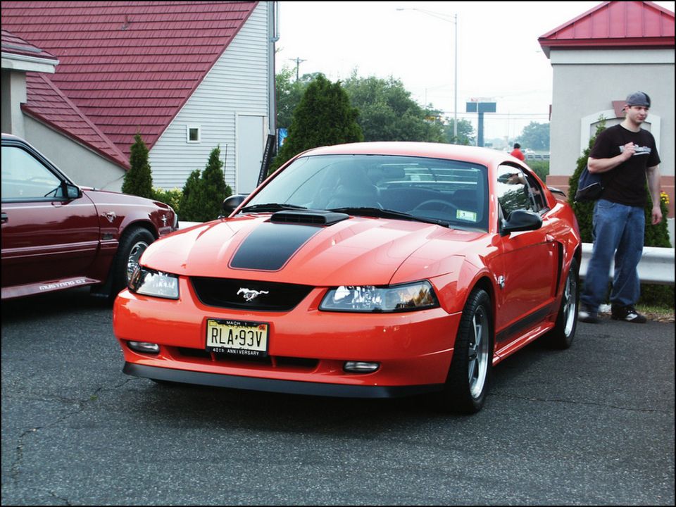 Orange Ford Mustang with black stripe on hood, front 3/4 view. License plate RLA-93V