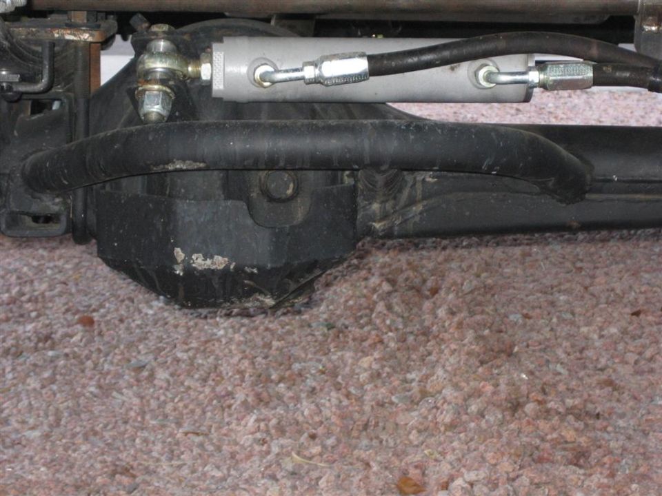 Power steering cylinder and linkage attached to front axle housing