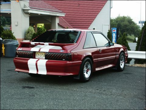 2001 Mercury Grand Marquis - A red Ford Mustang with racing stripes is parked outside a building.