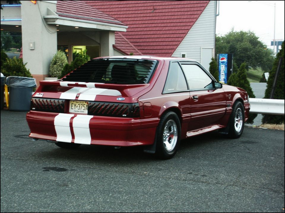 Red Ford Mustang with white racing stripes and louvers on the rear window
