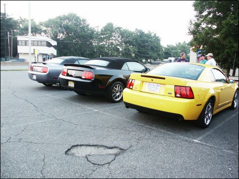 2001 Mercury Grand Marquis - Three Ford Mustangs, including a yellow coupe and a black convertible, are parked in a lot.
