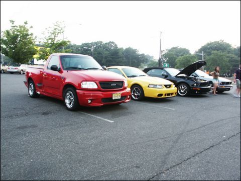 2001 Mercury Grand Marquis - Several cars are parked in a lot, including a red pickup truck and two Ford Mustangs.