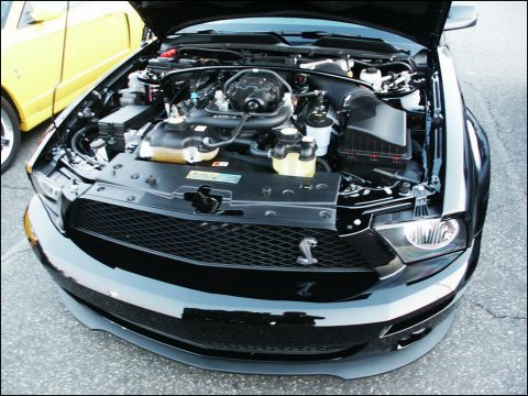 2001 Mercury Grand Marquis - The engine bay of a black Ford Mustang is visible, with a yellow vehicle partially seen in the background.