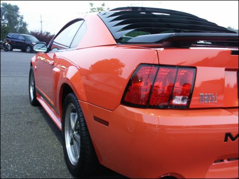 2001 Mercury Grand Marquis - Orange 2001 Ford Mustang Mach 1 with rear window louvers and a spoiler is seen from the rear quarter panel.