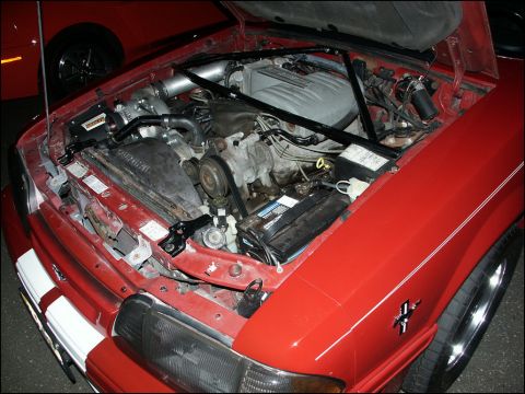 2001 Mercury Grand Marquis - The engine bay of a red car, a supercharger and strut tower brace, with another vehicle in the background.