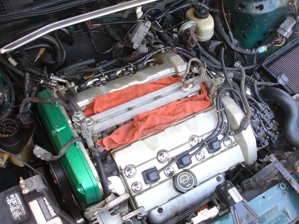 Engine bay with green valve cover, silver intake manifold, and orange rags. Oil cap visible
