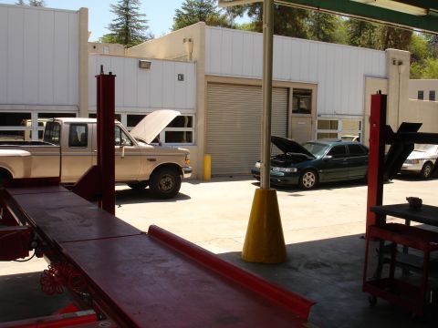 1993 Ford Taurus - A green 1993 Ford Taurus is parked with its hood open, alongside a pickup truck and another vehicle outside a service bay.