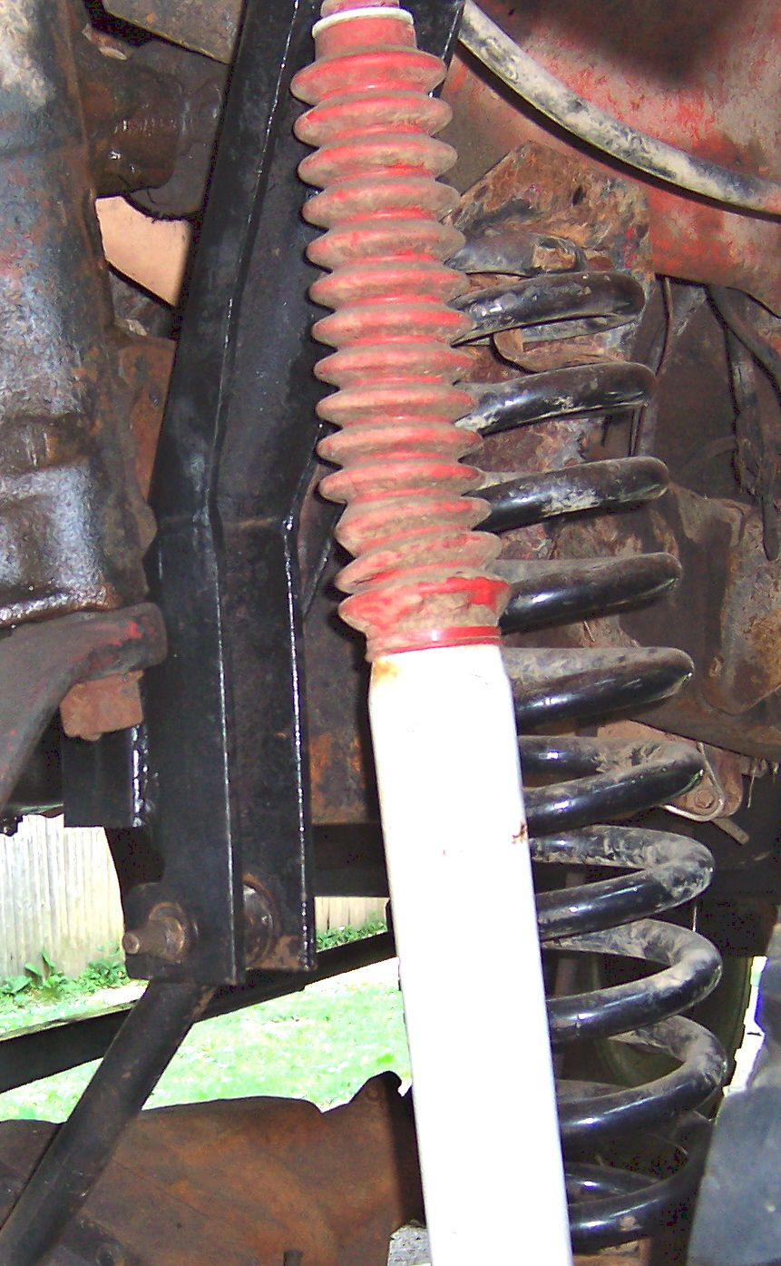 Close-up of a red-booted shock absorber and coil spring on a vehicle's suspension