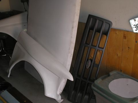 1990 Ford Bronco - A white fender and a black grille are stored indoors, possibly for a restoration project.