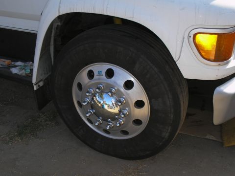 1999 Ford F-800 - The front wheel of a large truck, showing the tire and a polished aluminum hub. The vehicle's turn signal is visible.