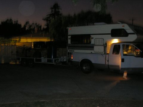 1989 Ford F-250 - A truck camper is parked with a trailer attached in the dim light of dusk.
