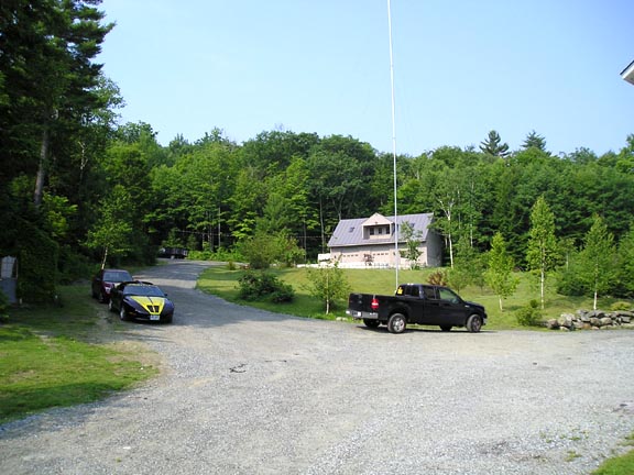 Yellow and black sports car parked on gravel drive with black pickup truck and house in background