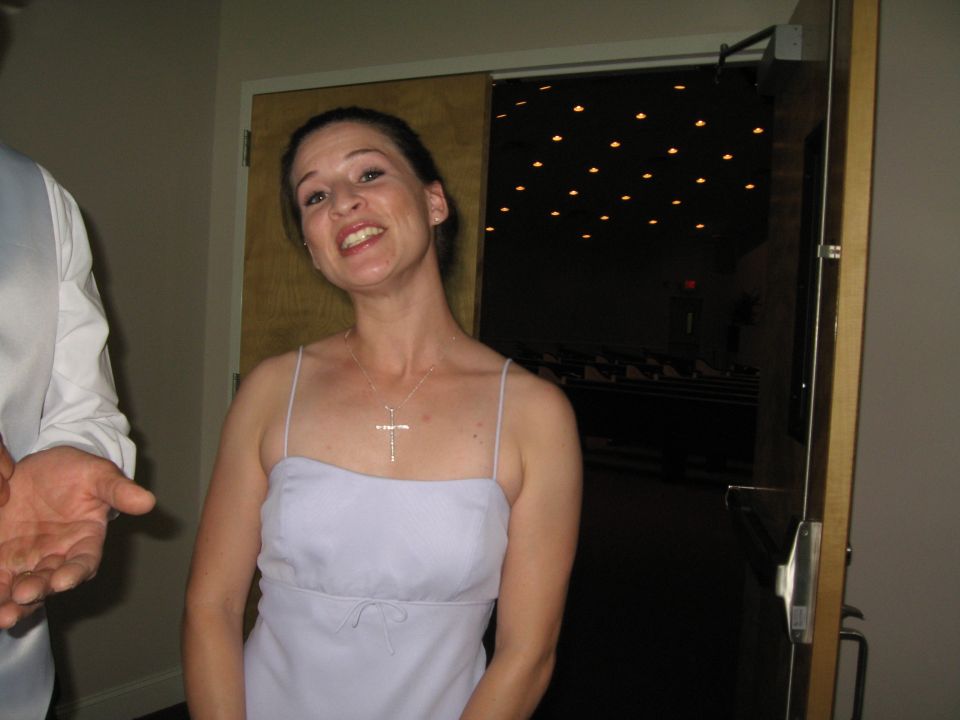Woman in a light purple dress with a cross necklace, standing indoors