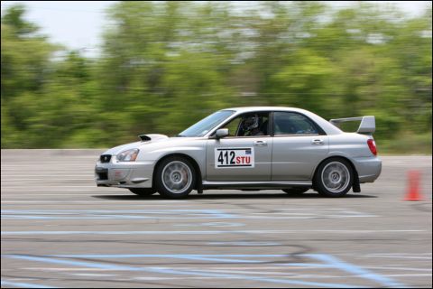 2001 Mercury Grand Marquis - A silver sedan with racing decals is captured in motion on a race track.