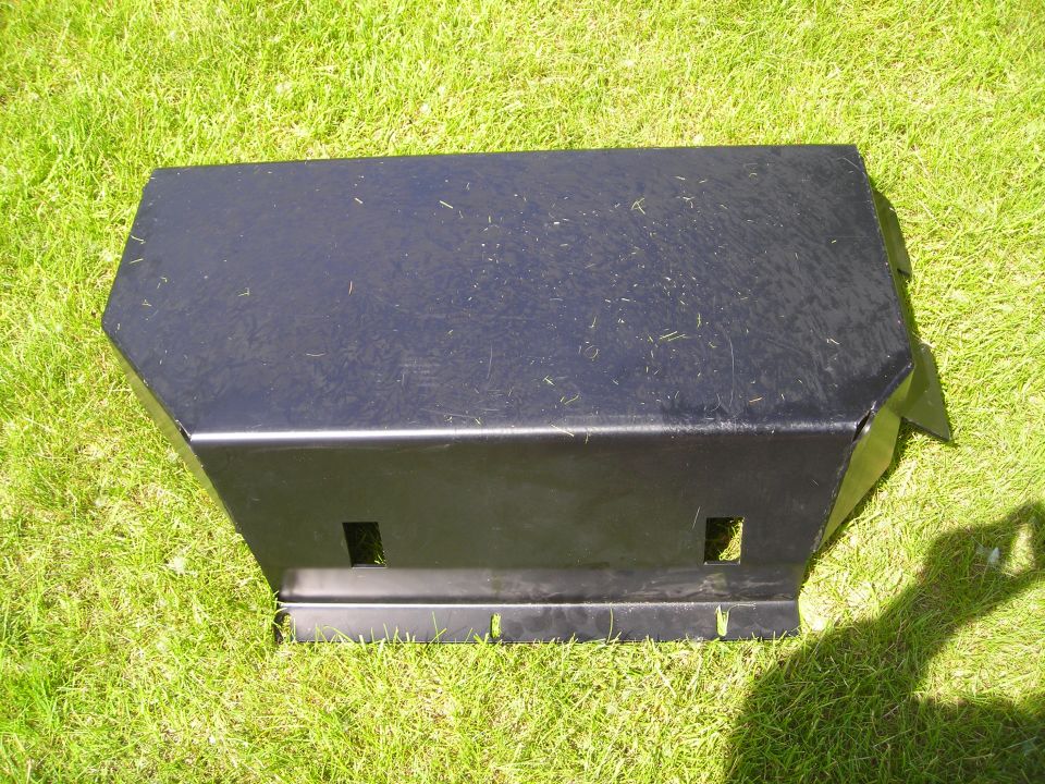 Black metal skid plate with two square cutouts on the front, lying on grass