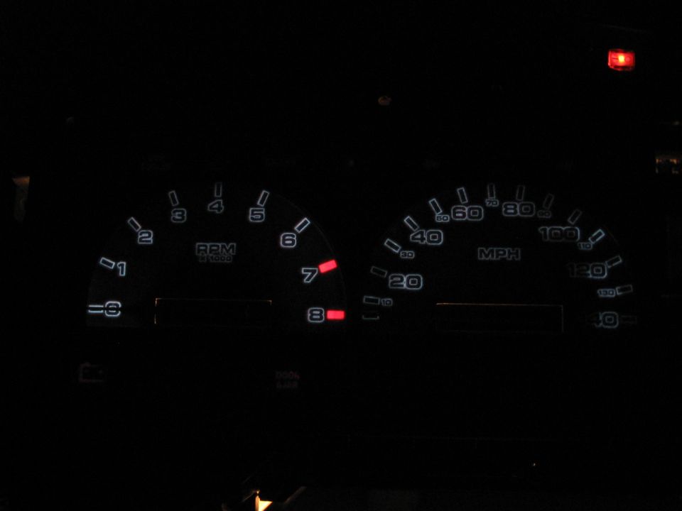Car dashboard with illuminated RPM and MPH gauges. Red indicator lights are visible