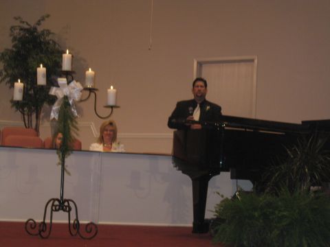 1988 Ford Bronco - A man speaks at a grand piano, with a candelabra and guests visible in the background.