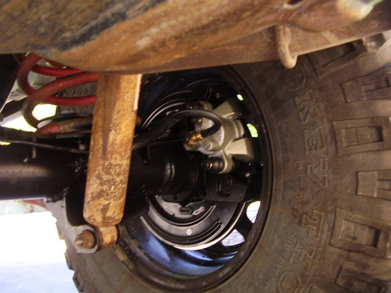 Rear axle and suspension with red coil spring and rusty shock absorber