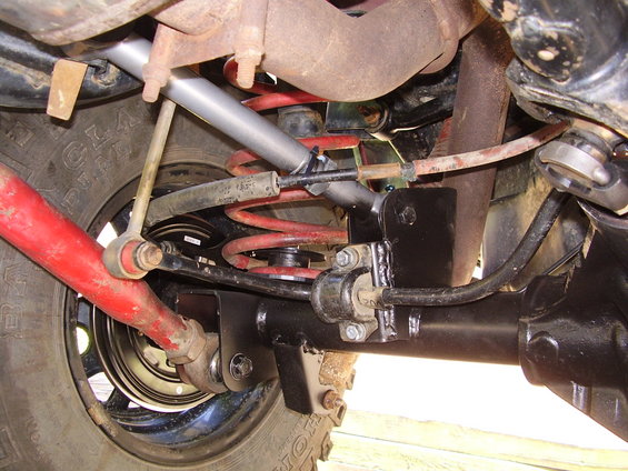 Close-up of Jeep Wrangler rear suspension with red control arms, black sway bar, and red coil springs