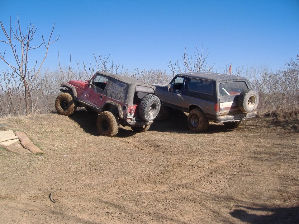Red Jeep Wrangler and a dark SUV on a dirt hill, both with off-road tires