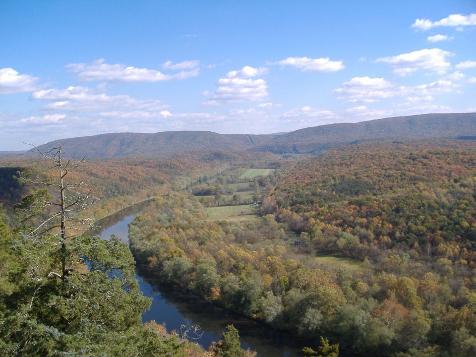 River valley with autumn foliage, distant mountains, and a bright blue sky with scattered clouds