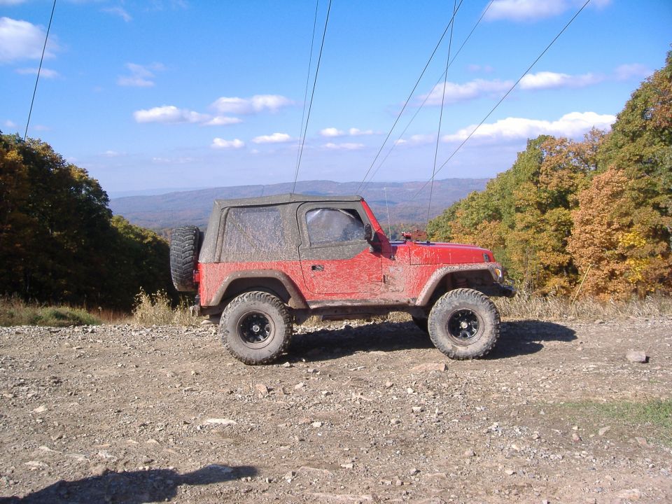 Red 2003 Jeep Wrangler parked on a dirt road with trees and mountains in the background