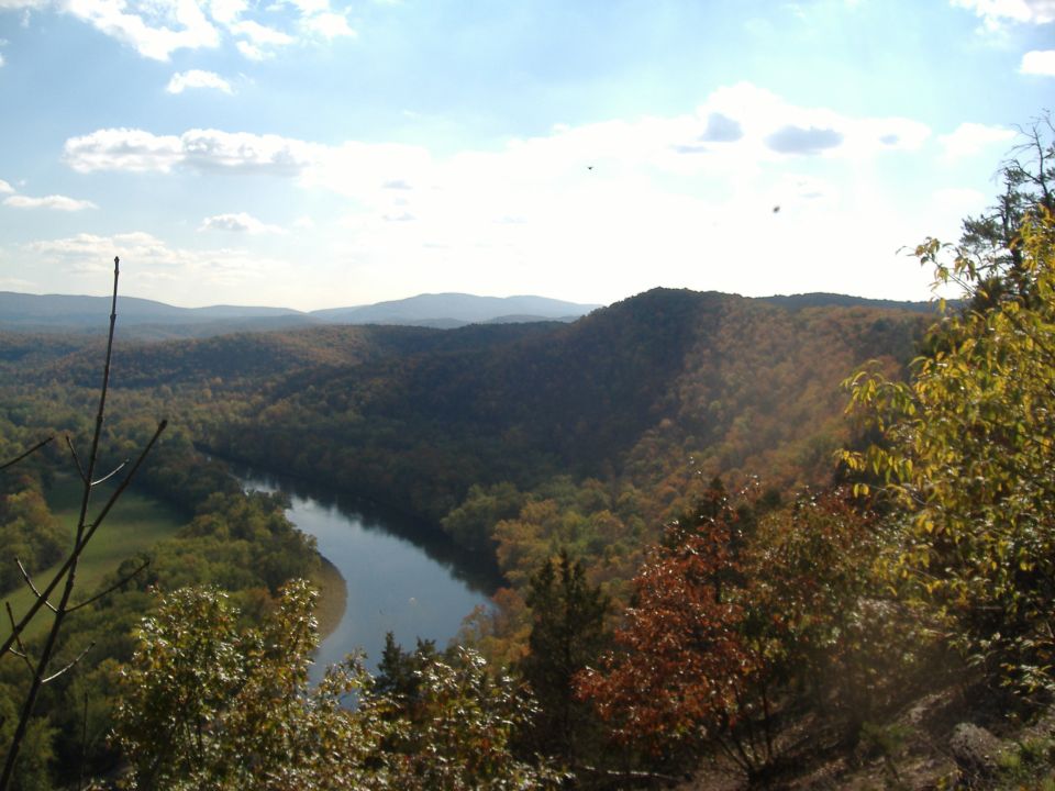 view of a river winding through a valley with hills and trees in autumn colors under a partly cloudy sky
