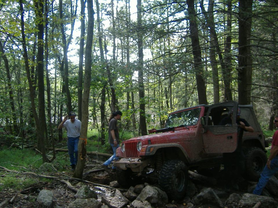 Red Jeep Wrangler with open doors on a rocky trail, tires deep in mud