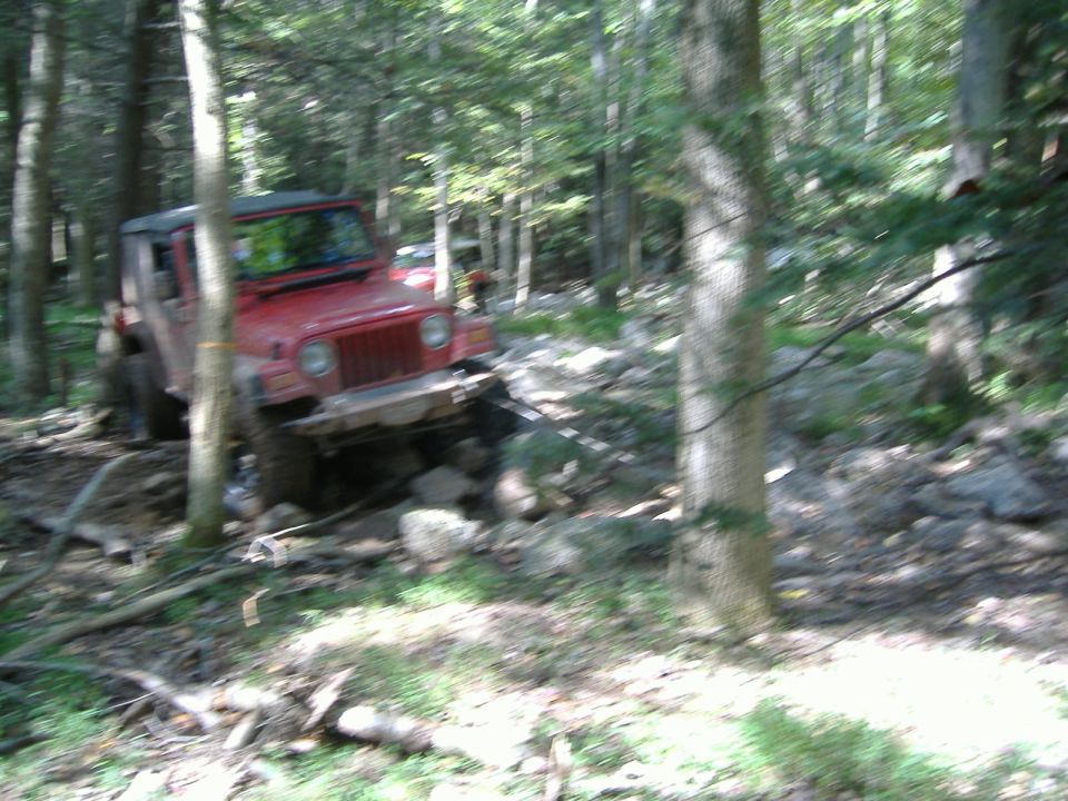 Red 2003 Jeep Wrangler navigating a rocky forest trail