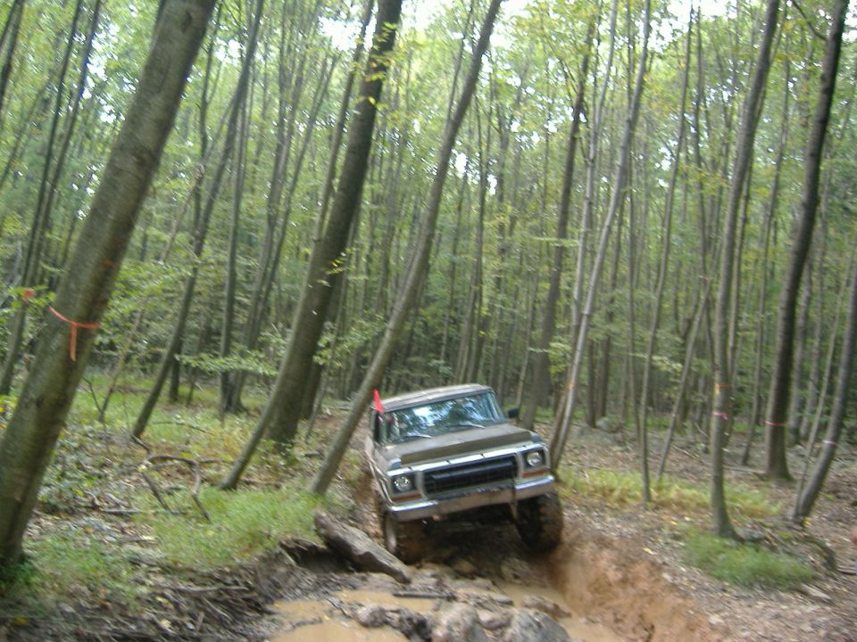 Brown 1970s Ford F-Series truck driving through a muddy trail in a forest