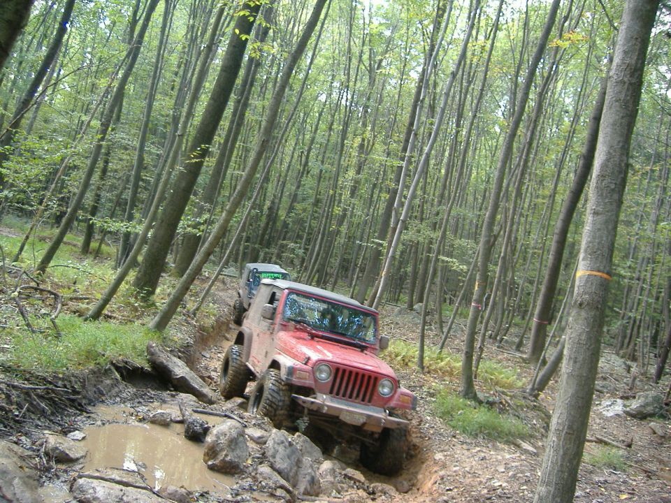 Red Jeep Wrangler navigating a muddy trail with another Jeep behind it