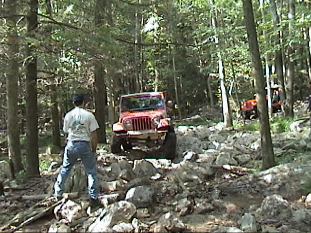 Red Jeep Wrangler driving on a rocky, wooded trail