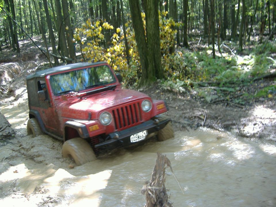 Red 2003 Jeep Wrangler stuck in mud on a wooded trail