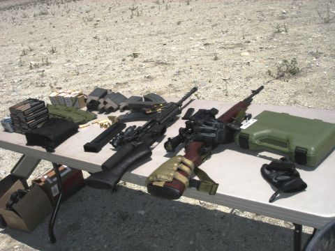 1990 Ford Bronco - Various firearms, magazines, and ammunition are laid out on a table at an outdoor location.