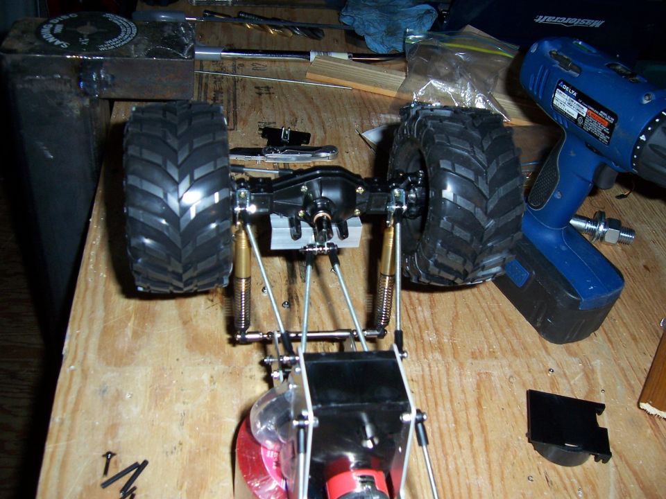 RC car chassis with large tires and suspension components, next to a blue drill