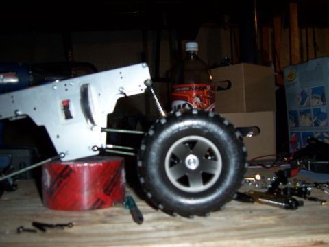 1996 Ford Bronco - A close-up of an RC car's chassis and wheel assembly, with various parts and a drink bottle in the background.