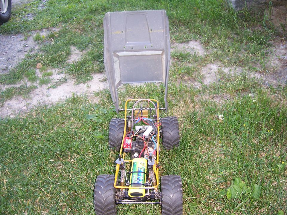 Remote control buggy chassis with large tires, exposed engine, and battery pack, with its body resting on top