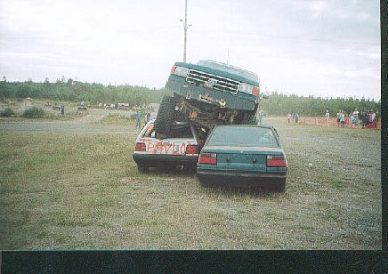 1989 Ford Bronco - A 1989 Ford Bronco is stacked on top of two sedans at an outdoor event.