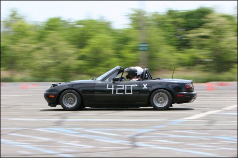 2001 Mercury Grand Marquis - A black convertible with racing numbers speeds around a track, with trees blurred in the background.