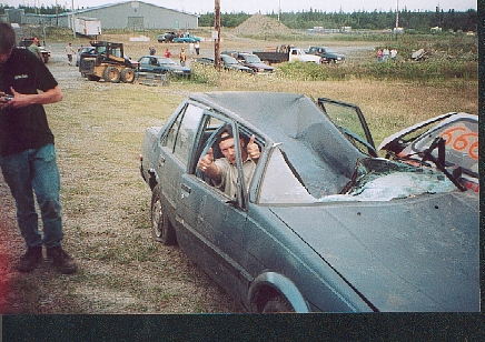 1989 Ford Bronco - A person in a heavily damaged sedan gives a thumbs up, with another vehicle partially visible in the background.