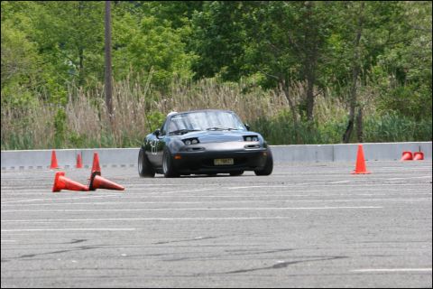2001 Mercury Grand Marquis - A black Mazda Miata navigates an autocross course, its pop-up headlights characteristic of the model.