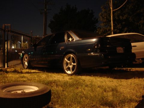 1993 Ford Taurus - A dark blue sedan with aftermarket wheels is parked on grass at night, with another vehicle partially visible behind it.