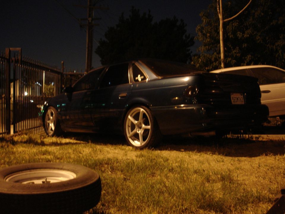 Dark sedan on grass at night with polished five-spoke wheels, spare tire in foreground