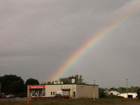 1978 Ford Mustang II - A vibrant rainbow arcs across a cloudy sky over a commercial building labeled 'The Beer Store'.
