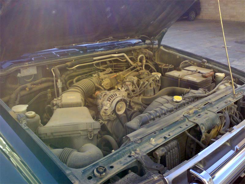 Dusty V6 engine bay of a teal SUV with hood up, showing air box, alternator, battery and radiator