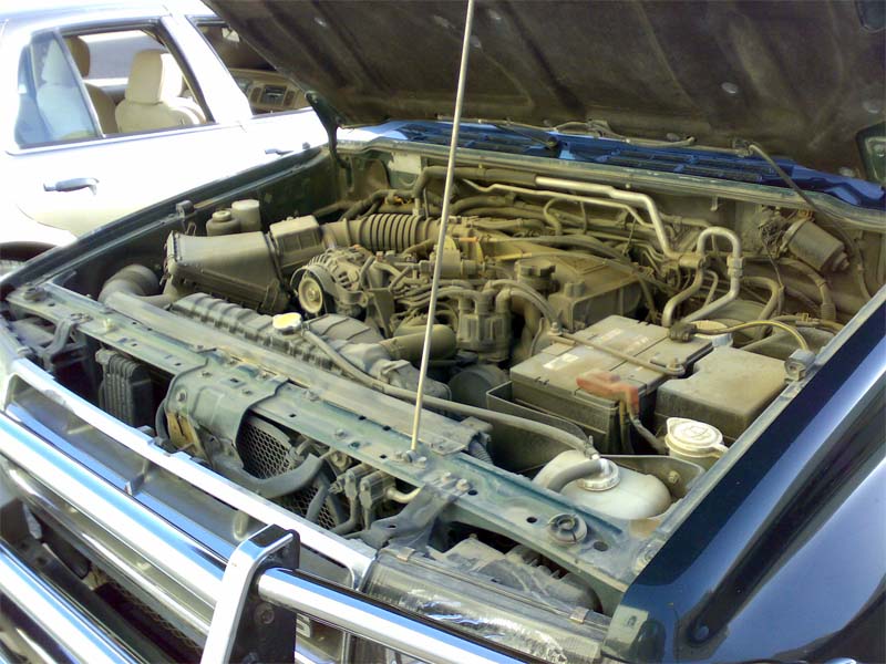 Dust-caked engine bay of a dark green SUV with hood open