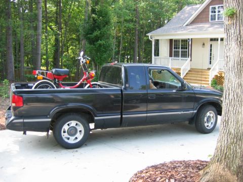 1985 Ford LTD Crown Victoria - A black pickup truck is parked in a driveway, with a red moped loaded into the truck bed.
