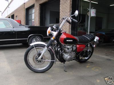 1985 Ford Crown Victoria LTD - A red and black Honda motorcycle is parked in front of a garage, with a black car to its left and another car in the background.