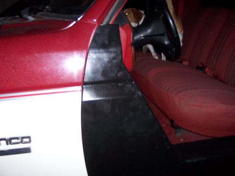 1991 Ford Bronco - A dog sits in the driver's seat of a red and white Ford Bronco, with the interior and part of the exterior visible.